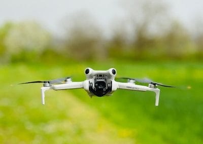 Image représentant un drone mini 4 pro de face survolant une prairie verte.